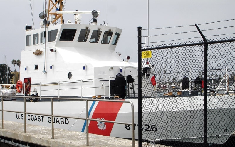 A US Coast Guard ship in the water next to a black chain-link fence installed by our commercial fencing company near Los Osos, California.